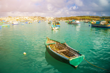 Marsaxlokk, Malta - Traditional green maltese Luzzu fisherboat at the old market of Marsaxlokk with green sea water, blue sky and palm trees on a summer day
