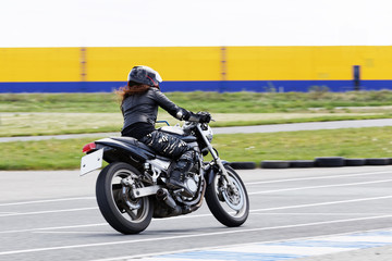 The red-haired girl in a black jacket and camouflage pants race on a motorcycle on a sports track. Motion blur.