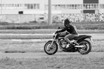 Fototapeta na wymiar The girl in a black jacket and grey pants race on a motorcycle. Motion blur. Black and white image.