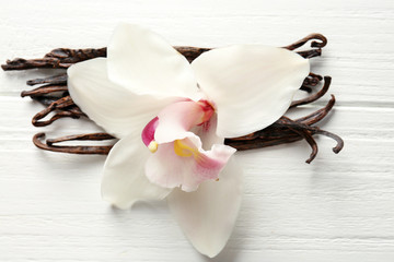 Fototapeta na wymiar Dried vanilla sticks and flower on light wooden background, closeup