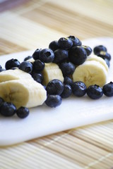 Bananas in slices and blueberries on a white board