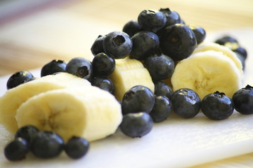 Bananas in slices and blueberries on a white board