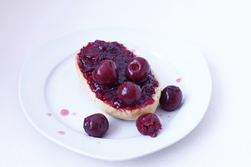 half bun with cherry jelly on a white plate, isolated