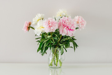 Bouquet of white and pink peonies in glass vase on white background