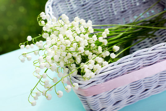 A bouquet of fresh white lilies of the valley in a wicker basket.
