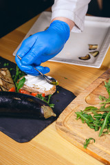 Chef hands with gloves cooked. Chef  is cooking a  gourmet dish - mozzarella with basil, cherry tomatoes with arugula and eggplant.