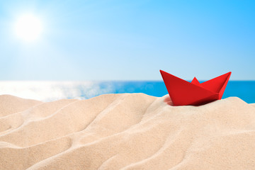 Fototapeta na wymiar On the Beach - red paper boat on a sand dune in front of beautiful azure sea on a sunny day