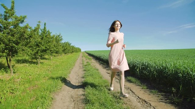 Pretty girl running on the path among wheat fields on early beautiful background