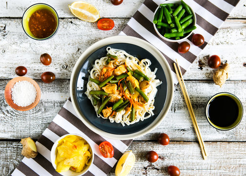 Asian lunch - udon noodles with chicken and vegetables with soy sauce on a wooden background, top view, flat