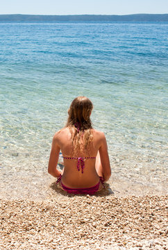 Vertical image of a young Caucasian female sitting at the edge of a shallow sea, looking at the horizon
