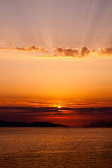 Fototapeta na wymiar panoramic image of golden sunset with sun low above the sea and sunrays coming through clouds above