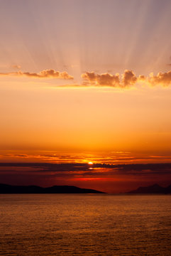panoramic image of golden sunset with sun low above the sea and sunrays coming through clouds above