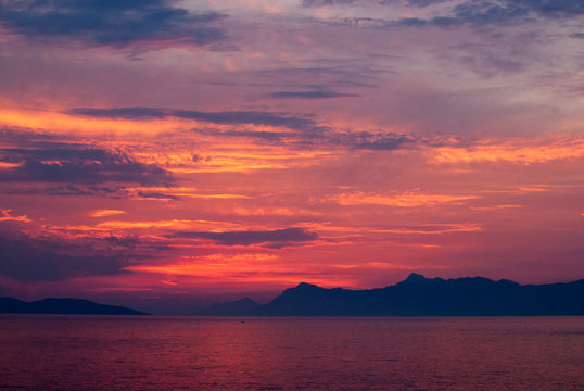 Fototapeta Horizontal image of deep coloured sunset with sea in red, golden and purple colours, black mountains on the horizon,