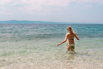 Young Caucasian female in bikini standing in shallow sea facing the horizon
