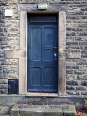 old faded black door with stone door frame and walls with wooden panels