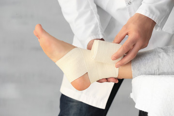 Doctor applying bandage onto patient's leg in clinic, closeup