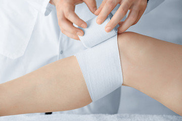 Doctor applying bandage onto patient's leg in clinic, closeup