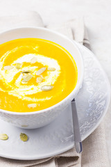 Carrot soup puree with coconut milk and pumpkin seeds on a marble background.
