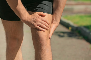 Young man suffering from pain in leg outdoors, closeup
