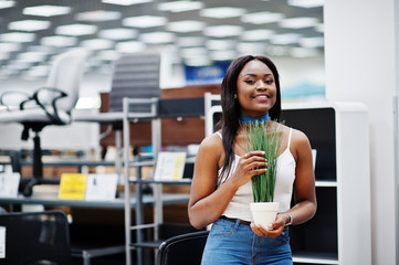 Stunning african american woman holding lovely small plant in the store.