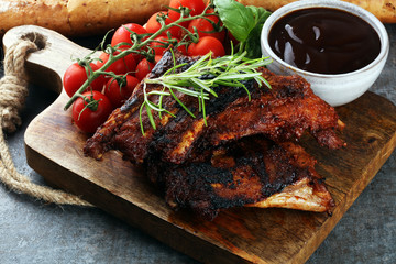 Spicy hot grilled spare ribs from a summer BBQ served with fresh tomatoes on an old vintage wooden cutting board