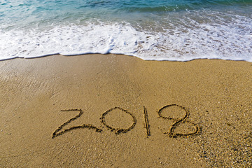 Handwritten number 2018 on a beach with waves - happy new year concept.