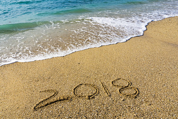 Handwritten number 2018 on a beach with waves - happy new year concept.