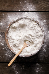 Bowl of white flour on white wooden table, top view