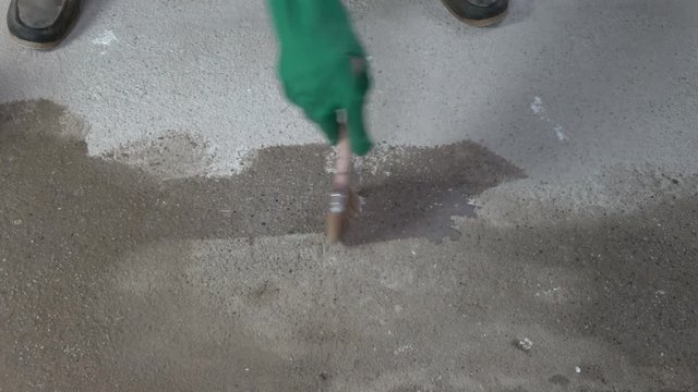 Worker with protective glove and  paintbrush covering concrete floor  primer 

