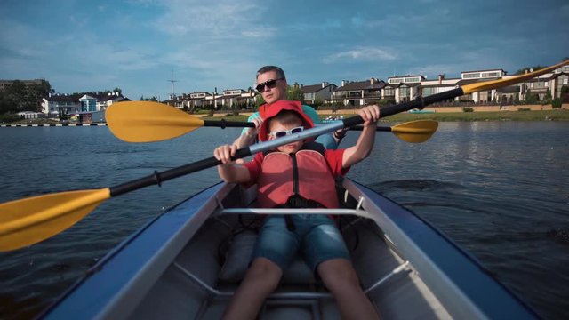 Little boy sitting in kayak with father and rowing.