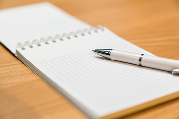 A notebook and ballpoint pen lying on a wooden table.