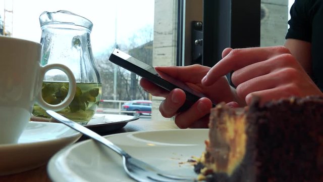 A man sits at a table with meal in a cafe and works on a smartphone - closeup, half-eaten pie in the foreground