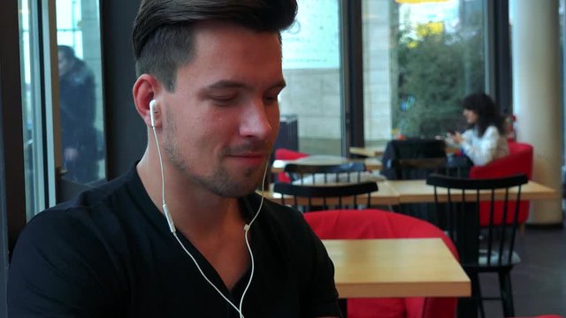 A young handsome man sits at a table with meal in a cafe and listens to music on a smartphone - closeup