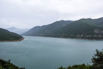 Живописное озеро в горах, водоем в горном ущелье между зеленых холмов, пасмурная погода, отдых на природе