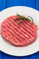 raw hamburger on white plate on wooden background