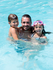 father playing in pool with two child boys and girl