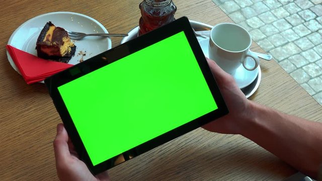A man holds a tablet with a green screen above a table with meal - closeup from above on the smartphone