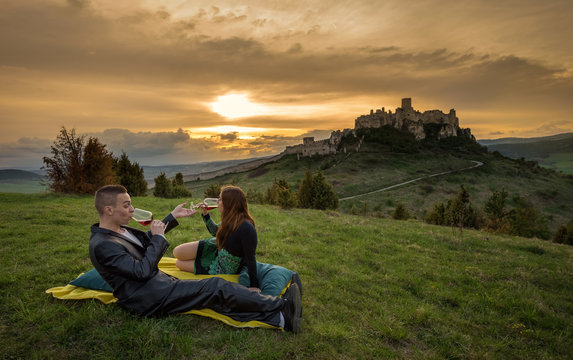 Couple drink red wine in nature under the ruins of a castle at sunset.