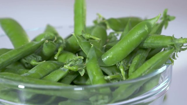 Heap of fresh raw green pea pods falling into a glass bowl in slow motion