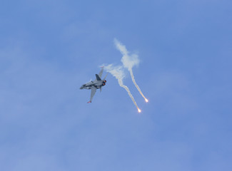Modern jet fighter flying against the blue sky and shooting flares.