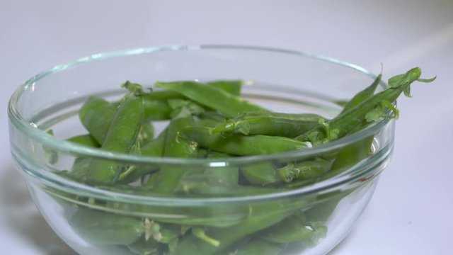 Closeup of fresh raw green pea pods falling into a glass bowl