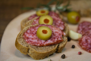 Delicious sandwiches with salami and olives on wooden board ready to eat