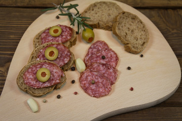 Delicious sandwiches with salami and olives on wooden board ready to eat