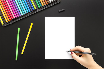 Black tabletop scene with female hand writing with a black pen on a white paper