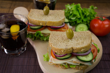 Sandwich with ham, cheese, tomatoes, lettuce, cucumbers and onions on a wooden background