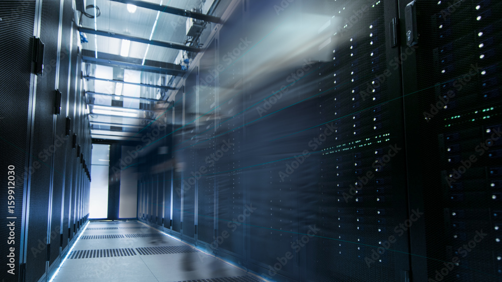 Poster shot of a working data center with rows of rack servers. people walk and work there, they are blurre
