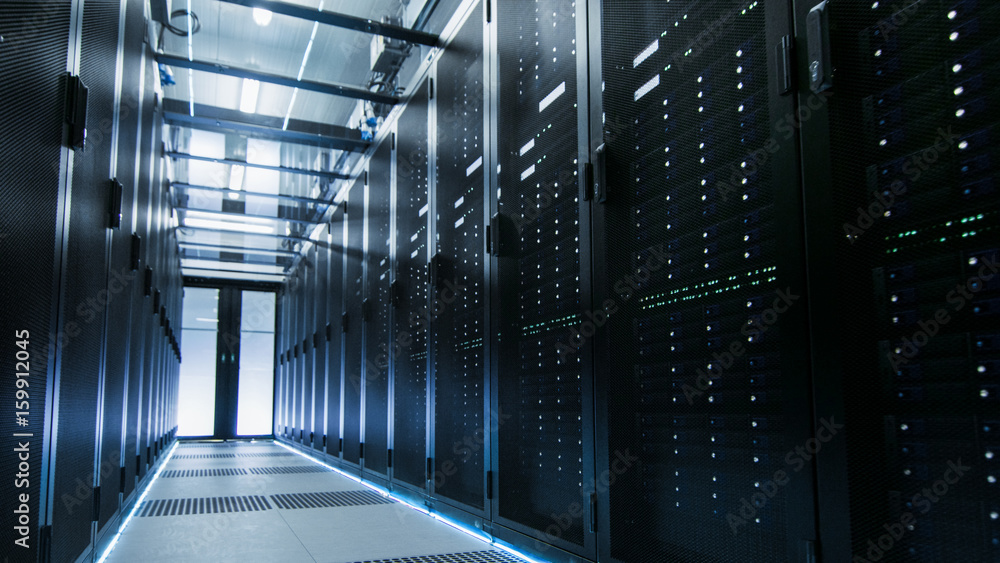 Poster shot of a working data center with rows of rack servers. people walk and work there, they are blurre