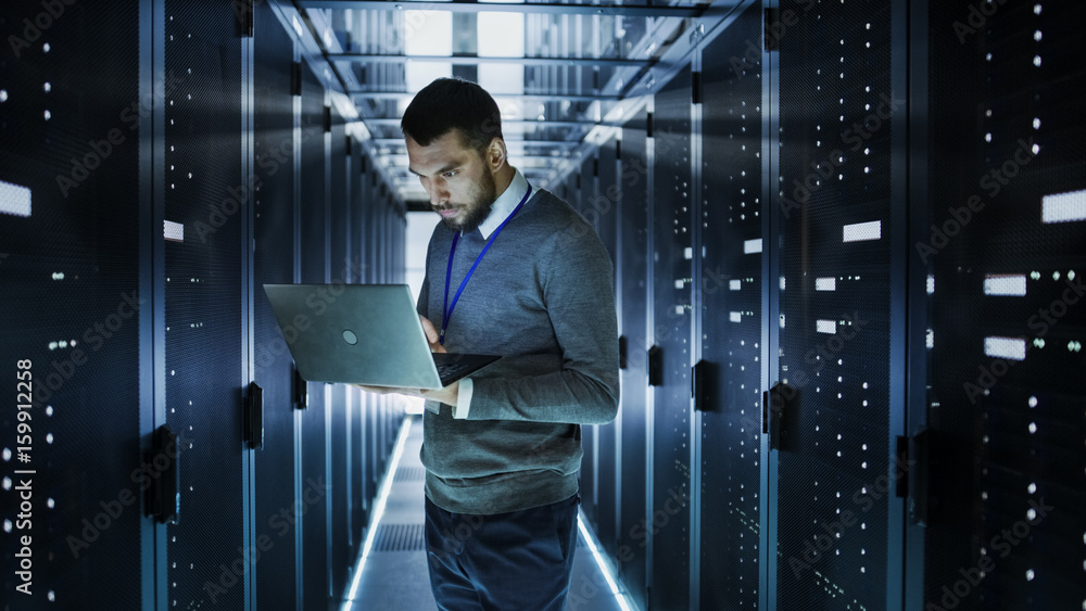 Poster it technician works on a laptop in big data center full of rack servers. he runs diagnostics and mai