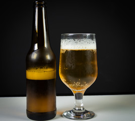 Glass of beer and beer bottle on a wooden background