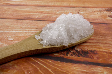 Sea salt in a wooden spoon. Also called bay salt or solar salt, is used in cooking and cosmetics. Rough grained crystals of the mineral.
